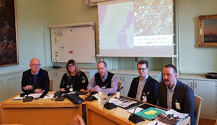 Fem personer på ett podium, ovanför dem en presentation.