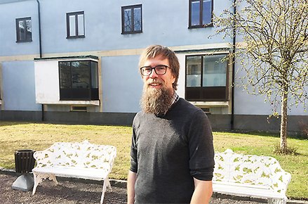 Per Jonsson ståendes utomhus med det blå stadshuset i bakgrunder och grönskande björk på sidan.