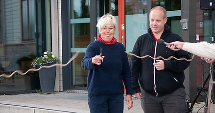 En kvinna klipper av ett band med sax. En man står bredvid.