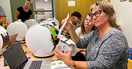 Två kvinnor arbetar koncentrerat med att fylla på en läkemedelsautomat som står på bordet framför dem.