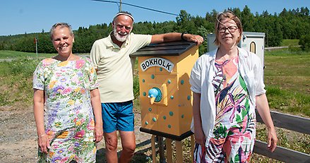 tre personer som står vid ett skåp med en träfågel på