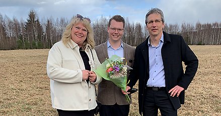 en kvinna och två män står på en åker. en av männen håller en blombukett i handen.