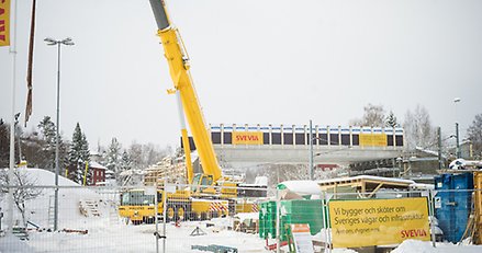 Byggarbetsplats för en ny bro, med bron i bakgrunden och en kranbil