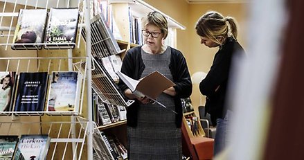 En bibliotekarie och en besökare i biblioteket.