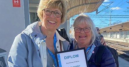 Två glada kvinnor står utomhus och håller upp ett diplom.