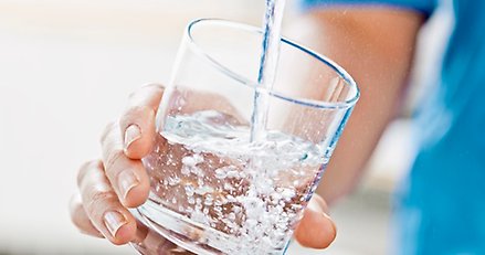 en hand håller ett vattenglas som fylls på under en vattenkran 
