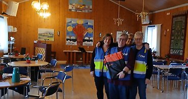 Tre leende kvinnor i reflexvästar står inomhus.