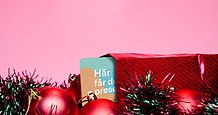 ett presentkort sticker ut ur ett paket som ligger bland glitter och julkulor.