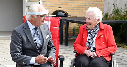 man med visir sitter bredvid en skrattande äldre kvinna i en rullstol