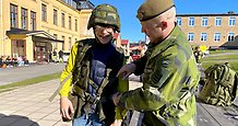 En man i grön uniform hjälper en gymnasieelev att ta på sig militär utrustning.