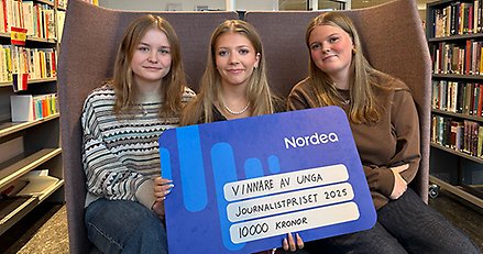 tre unga kvinnor sitter i en soffa med en stor prischeck i handen