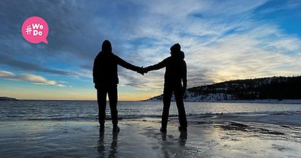 två personer sedda bakifrån står på en strand vid havet och håller varandra i handen