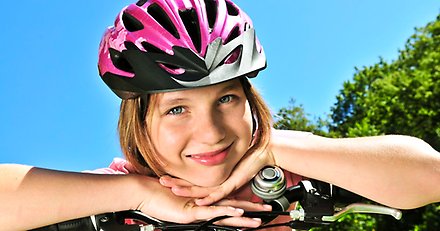 flicka med cykelhjälm som lutar sig med armarna mot styret
