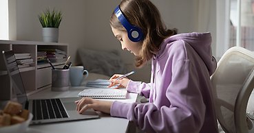 Ung tjej som sitter vid en dator och gör anteckningar i ett block.