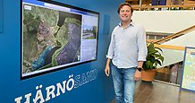 Leende ung man står framför en digital skärm som visar en karta. Under skärmen står textat HÄRNÖSAND.