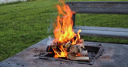 eld i eldstad intill älv med parkbänk bredvid