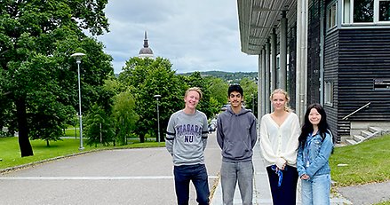 Två killar och två tjejer står vid sambiblioteket i Härnösand med stadsparken och domkyrkan i fonden.