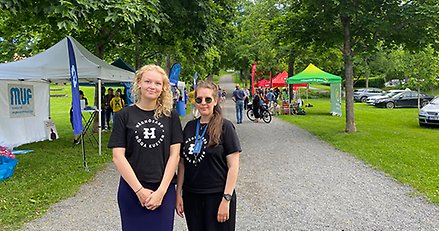 Två kvinnor i stadsparken med tält från olika politiska partier i bakgrunden.