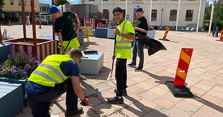 Fyra unga killar med varselvästar rensar ogräs på torget.