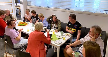 Ett tiotal personer i olika åldrar samlade runt ett fikabord.