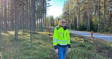 en man med reflexgul jacka står i en skog vid sidan om en väg
