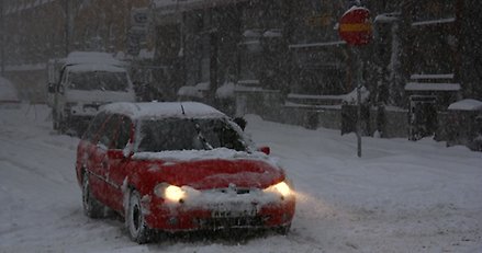 en röd bil i snöoväder i en gatumiljö med mycket snö