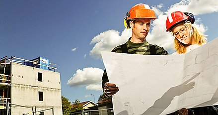 En man och en kvinna som läser ritningar på en byggarbetsplats.