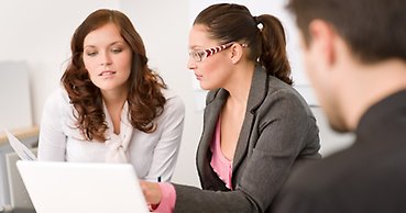 Tre personer samarbetar runt en dator på ett kontor.