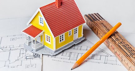 en modell av ett hus, en tumstock och en blyertspenna ligger på en ritning av ett hus