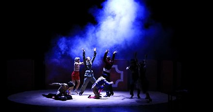 en scen med flera dansare och rök i ett blått ljus