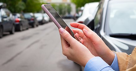 person håller telefon i handen, parkerade bilar på en gata