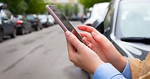 person håller telefon i handen, parkerade bilar på en gata