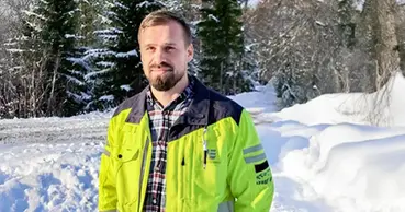 Morgan Rönnlund står i gul varseljacka, i bakgrunden ser man skog och snö. 