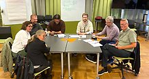 Sju personer sitter och skriver runt ett bord i en konferenslokal.