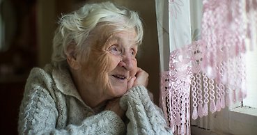 en äldre kvinna tittar ut genom ett fönster