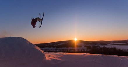 en skidåkare har lämnat ett hopp och gör en volt i luften mot en himmel med solnedgång