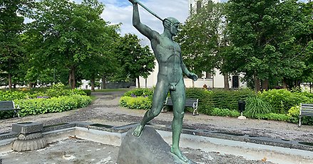 skulptur av en naken mansfigur med ett ljuster höjt i den högra handen