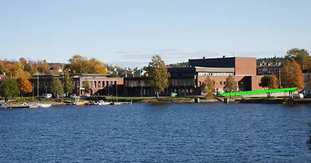 vy över en stor röd byggnad med vatten i förgrunden. intill byggnaden går ett grönt streck