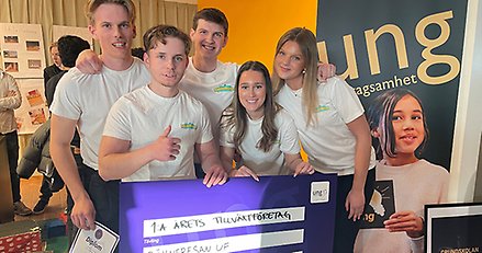 Fem glada ungdomar som poserar vid en stor prischeck.