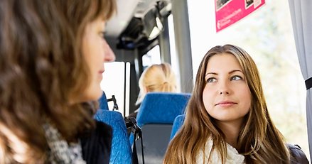 två kvinnor sitter i en buss och er på varandra