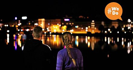 Två personer intill varandra står och blickar in mot Härnösands centrum. Kvällstid.