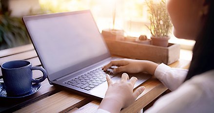 Genrebild som visar en oidentifierbar person som sitter och arbetar på sin laptop vid ett fönster.