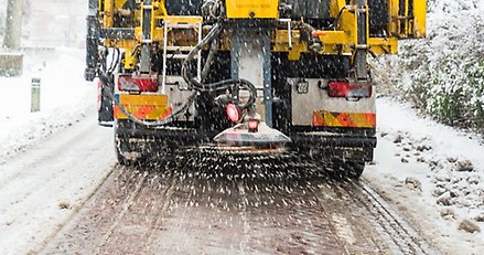 en gul lastbil med en saltspridare baktill