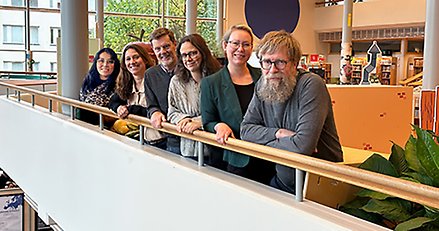 flera personer på rad som lutar sig över ett räcke och tittar in i kameran.