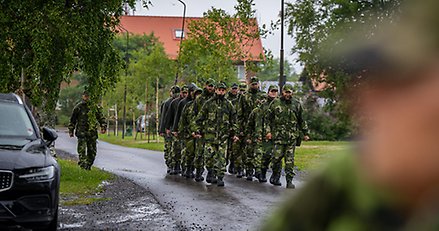 Omkring femton personer i gröna militära kamouflagekläder marscherar på två led.