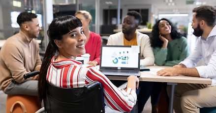 sex vuxna sitter runt ett bord. En av dem har en dator framför sig och vänder sig mot kameran och ler.