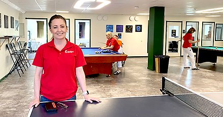 En kvinna i i vårdkläder i förgrunden. I bakgrunden två biljardbord där några personer spelar.