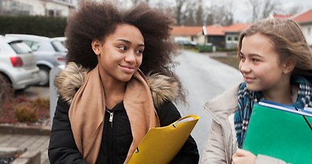 två flickor som är på varsin mapp går på en väg