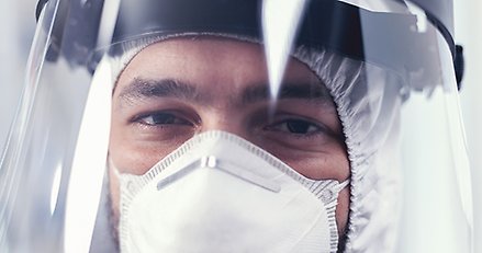 närbild på person med munskydd och visir