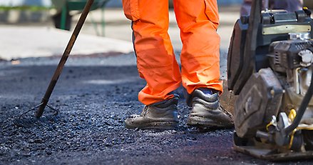 benen på en person med orange byxor som skrapar asfalt på en väg